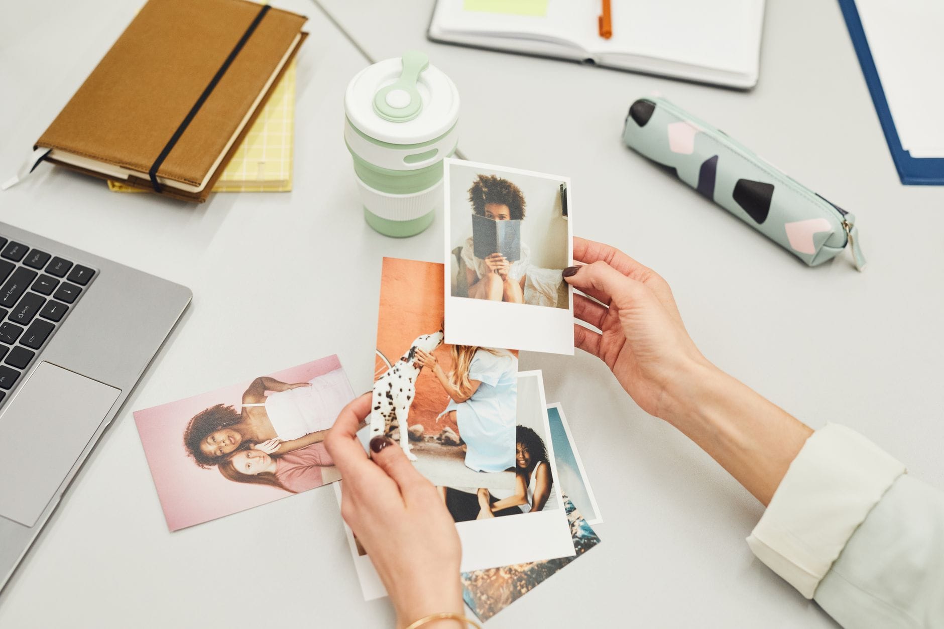 Jak poprawnie przygotować zdjęcia do fotoksiążki, aby uzyskać najlepszą jakość druku Dłonie przeglądające zdjęcia polaroid na biurku z materiałami kreatywnymi